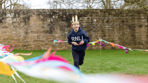 Boy running through colourful bunting with his egg and spoon.